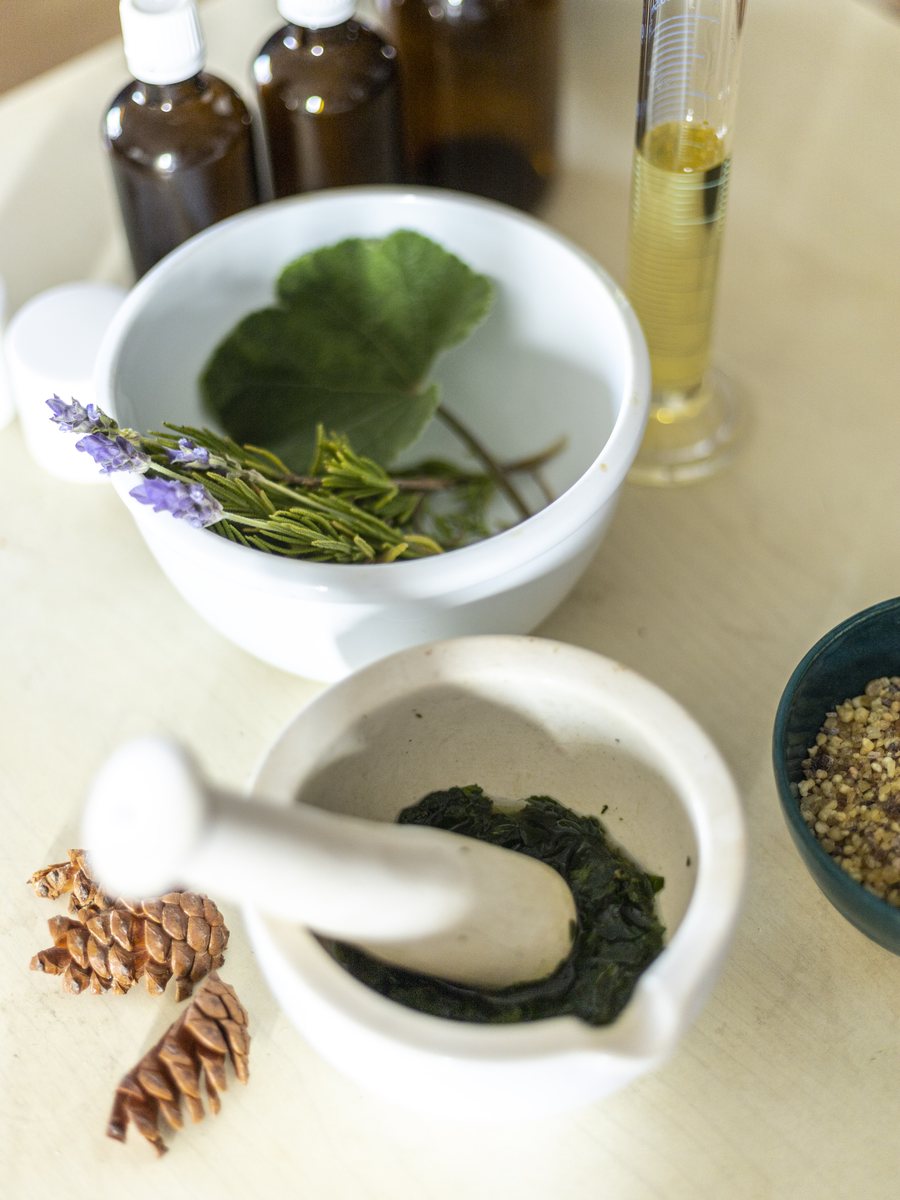 A mortar and pestle with lavender, rosemary, and herbal tinctures.